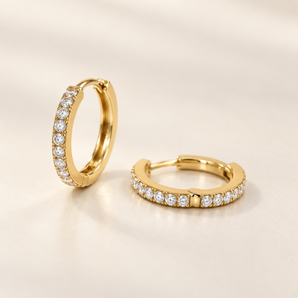 EVELYNNIE pavé huggie hoop earrings in yellow gold on a warm ivory background